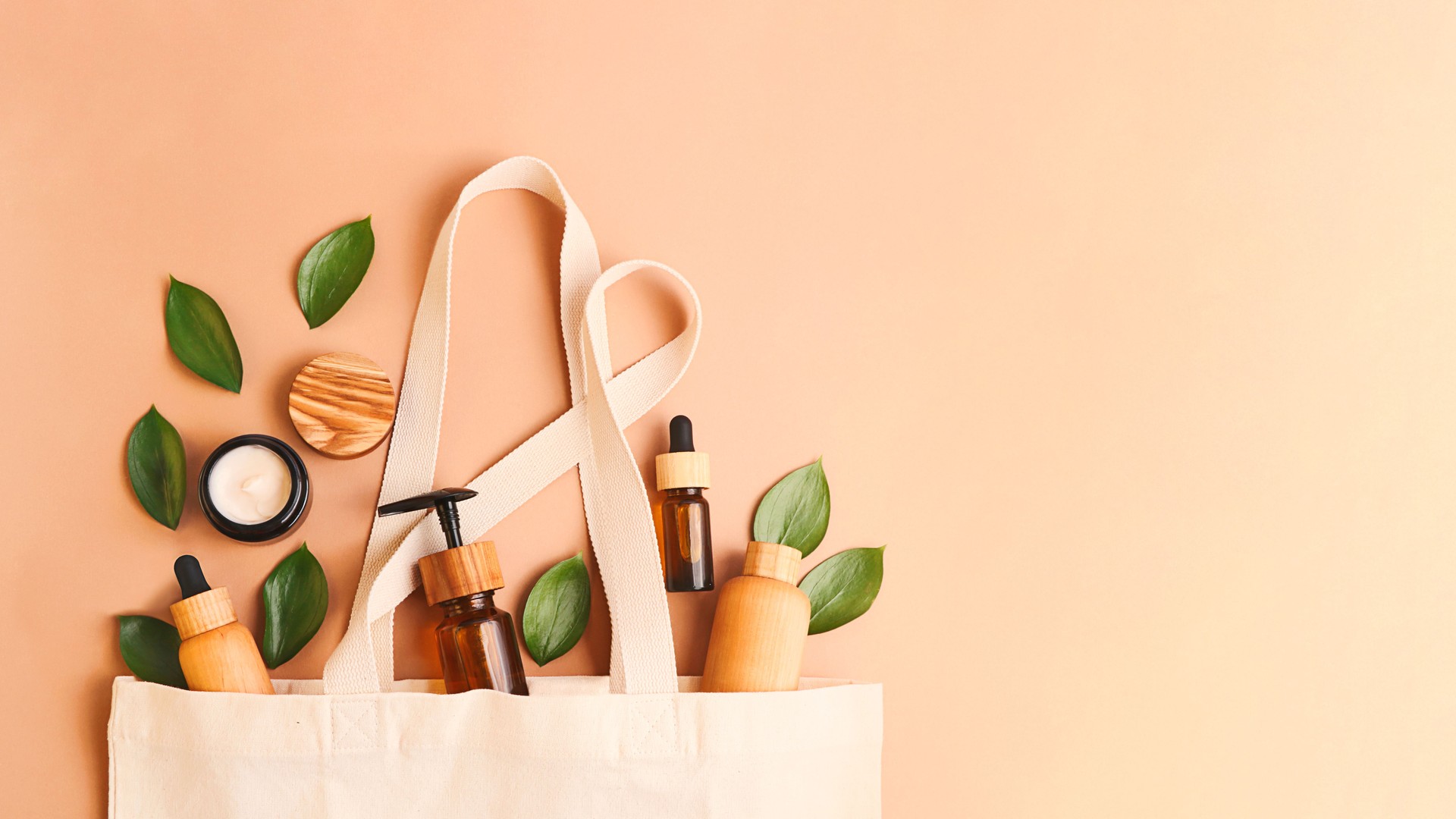 Open eco friendly cotton reusable bag with different containers from natural wood and brown glass.Fresh leafs around.Concept of organic,zero waste cosmetics.Woman bag with accessories,large banner.